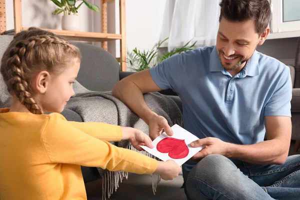 Happy man receiving greeting card from his little daughter at home
