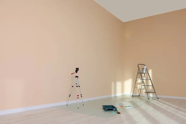 Stepladder, laser level and painting tools near wall in empty room, space for text
