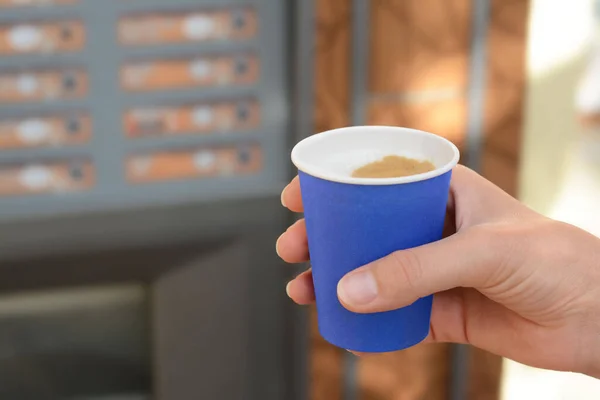 Woman holding paper cup with coffee near vending machine, closeup. Space for text