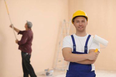 Worker holding paint roller in unfinished room. Painting walls