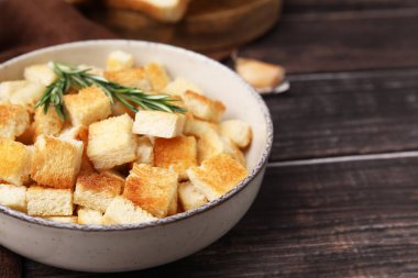 Delicious crispy croutons with rosemary in bowl on wooden table, closeup