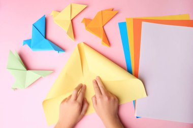 Origami art. Child folding paper on pink background, closeup and top view