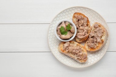 Tasty sandwiches with cod liver and parsley on white wooden table, top view. Space for text