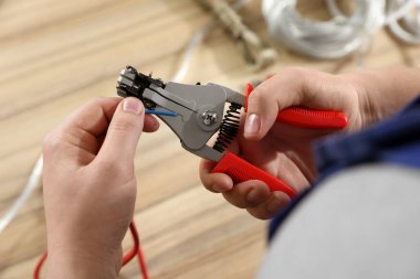 Professional electrician stripping wiring at wooden table, above view