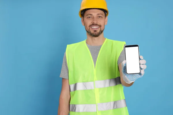 Male industrial engineer in uniform with phone on light blue background