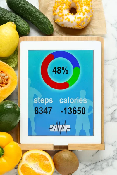 Tablet with weight loss calculator application and food products on white marble table, flat lay