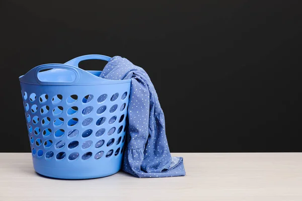 Plastic laundry basket with clothes near dark grey wall. Space for text