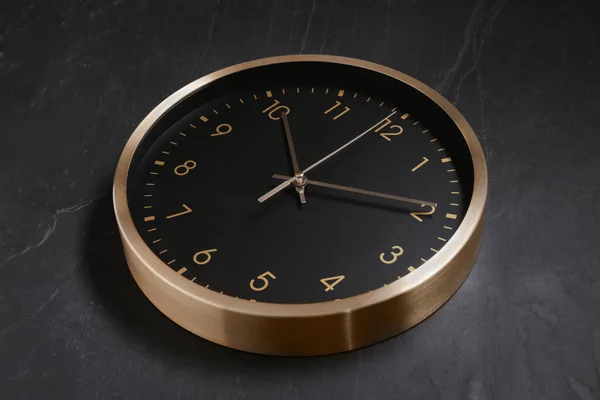 Stylish round clock on black table, closeup. Interior element