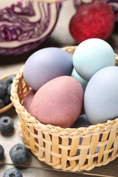 Colorful Easter eggs painted with natural dyes in wicker bowl on wooden table, closeup