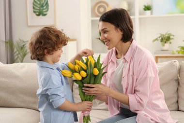 Happy woman with her cute son and bouquet of beautiful flowers at home. Mother's day celebration