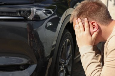 Stresli bir adam arabanın yanında, açık havada çizik var.