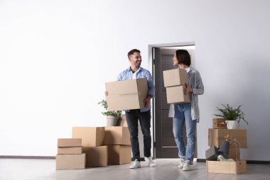 Happy couple with moving boxes entering in new apartment