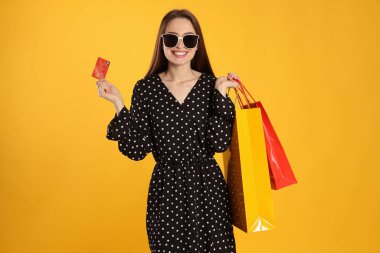 Happy young woman with shopping bags and credit card on yellow background. Big sale