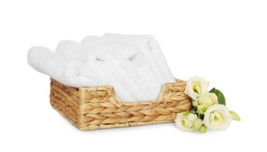 Wicker basket with folded soft terry towels and flowers on white background