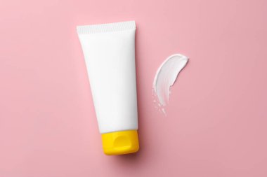 Tube of face cream and sample on pink background, top view