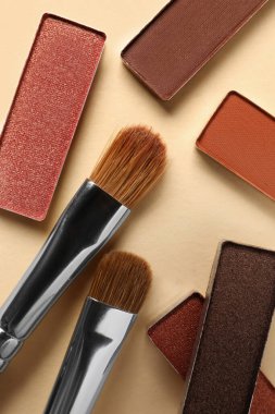 Different beautiful eye shadows and makeup brushes on beige background, flat lay