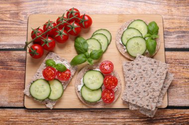 Tasty crispbreads, cucumber, tomatoes and basil on wooden table, top view