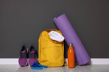 Backpack and sports equipment on floor near gray wall