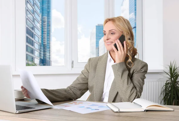 オフィスの机の上でスマートフォンで話している論文と女性の上司 成功した実業家 — ストック写真
