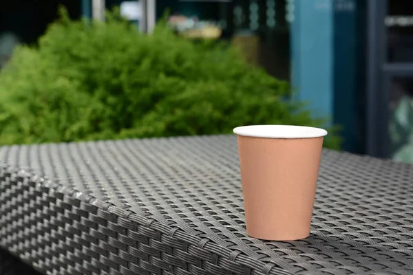 Coffee cardboard cup on rattan table outdoors, space for text