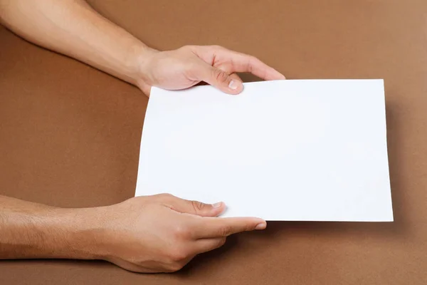 Man Holding Sheet Paper Brown Background Closeup Mockup Design — Stock fotografie