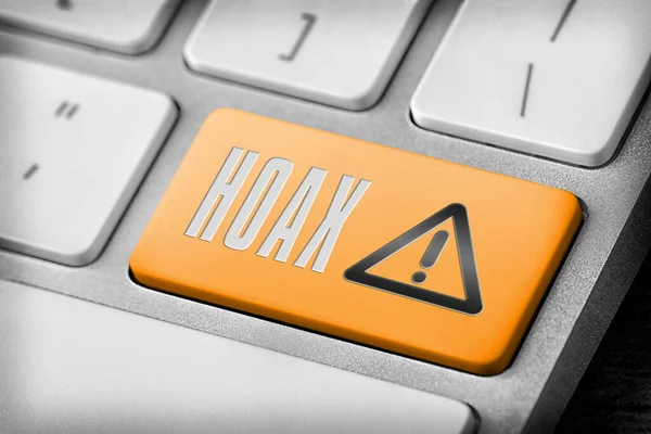 Orange button with word Hoax and warning sign on computer keyboard, closeup