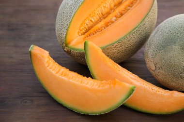Whole and cut delicious ripe melons on wooden table, closeup