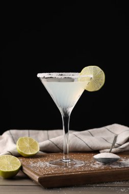 Martini glass of refreshing cocktail with lime and sugar on wooden table against black background