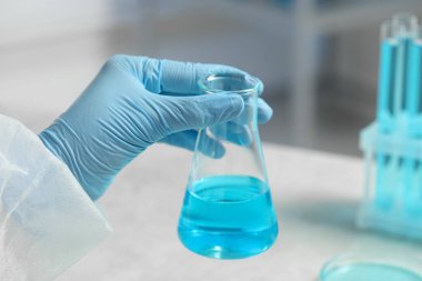 Laboratuvarda açık mavi sıvıyla çalışan bilim adamı, yakın plan.