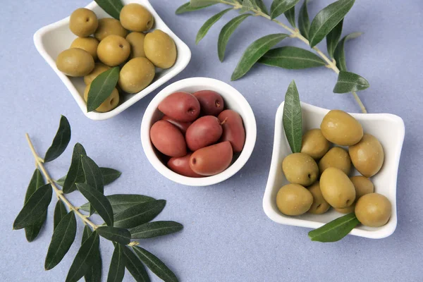 Different fresh olives and leaves on violet background, flat lay