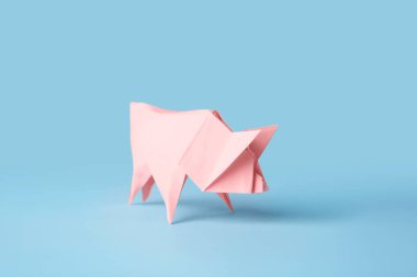 Origami sanatı. Açık mavi arka planda el yapımı pembe kağıt domuz.