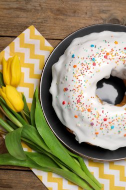 Easter cake with sprinkles and tulips on wooden table, flat lay