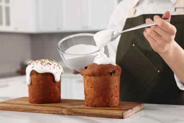 Woman decorating traditional Easter cake with glaze at white marble table in kitchen, closeup