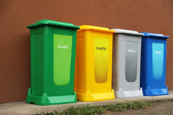 Many color recycling bins near brown wall outdoors