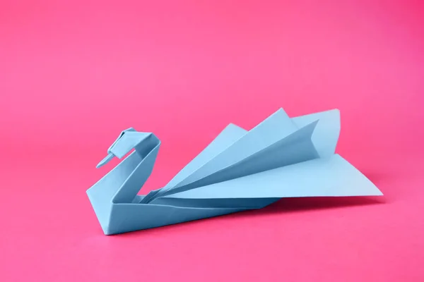 Light blue paper swan on pink background. Origami art