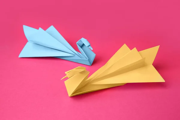 Paper swans on pink background. Origami art