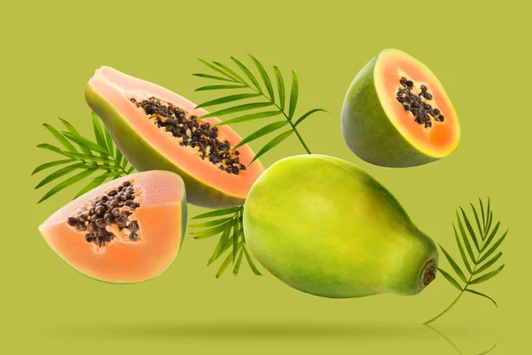 Fresh papaya fruits and leaves falling on bright green background