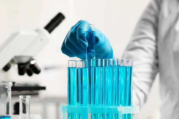 Scientist taking test tube with light blue liquid in laboratory, closeup