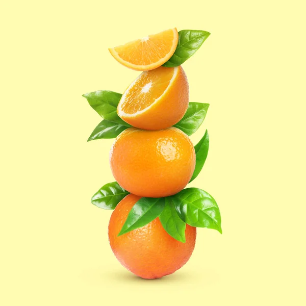 Gestapelt Geschnittene Und Ganze Orangen Mit Grünen Blättern Auf Hellgelbem — Stockfoto