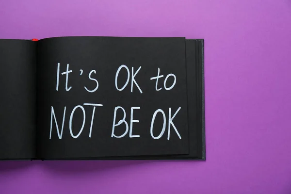Notebook with phrase It`s Ok To Not Be Ok on purple background, top view