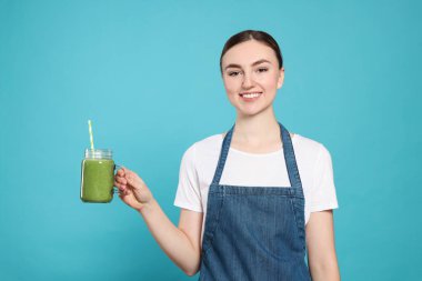 Kot önlüklü güzel bir kadın açık mavi arka planda leziz bir smoothie ile