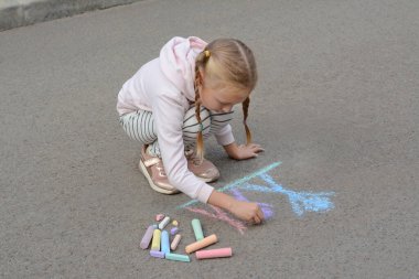 Küçük çocuk asfalta tebeşirle mutlu bir aile çiziyor.