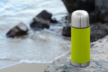 Metalik termos sıcak içecekle deniz kenarında taş üstünde, metin için boşluk