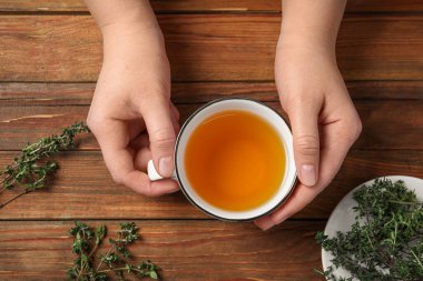 Ahşap masada aromalı kekik çayı olan kadın, üst manzara.