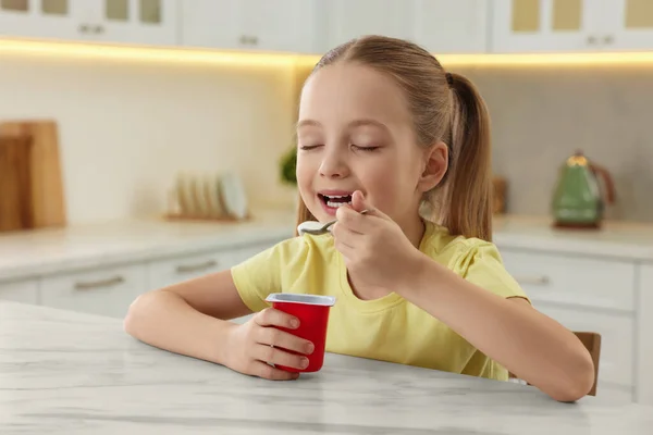可爱的小女孩在厨房的白色大理石桌上享用美味的酸奶 — 图库照片