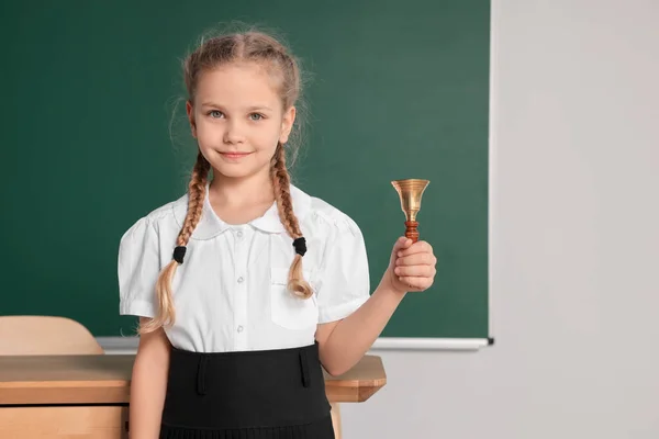 Pupil with school bell near chalkboard in classroom