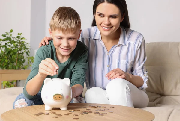 男の子とともに彼の母親置くコインに貯金箱に自宅 — ストック写真