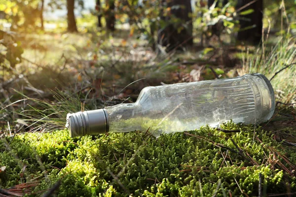 stock image Used glass bottle on grass in forest. Recycling problem