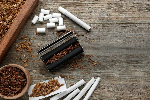 Stock image Flat lay composition with roller and tobacco on old wooden table, space for text. Making hand rolled cigarettes