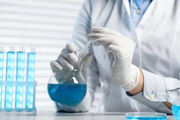 stock image Scientist taking sample of light blue liquid at white table in laboratory, closeup